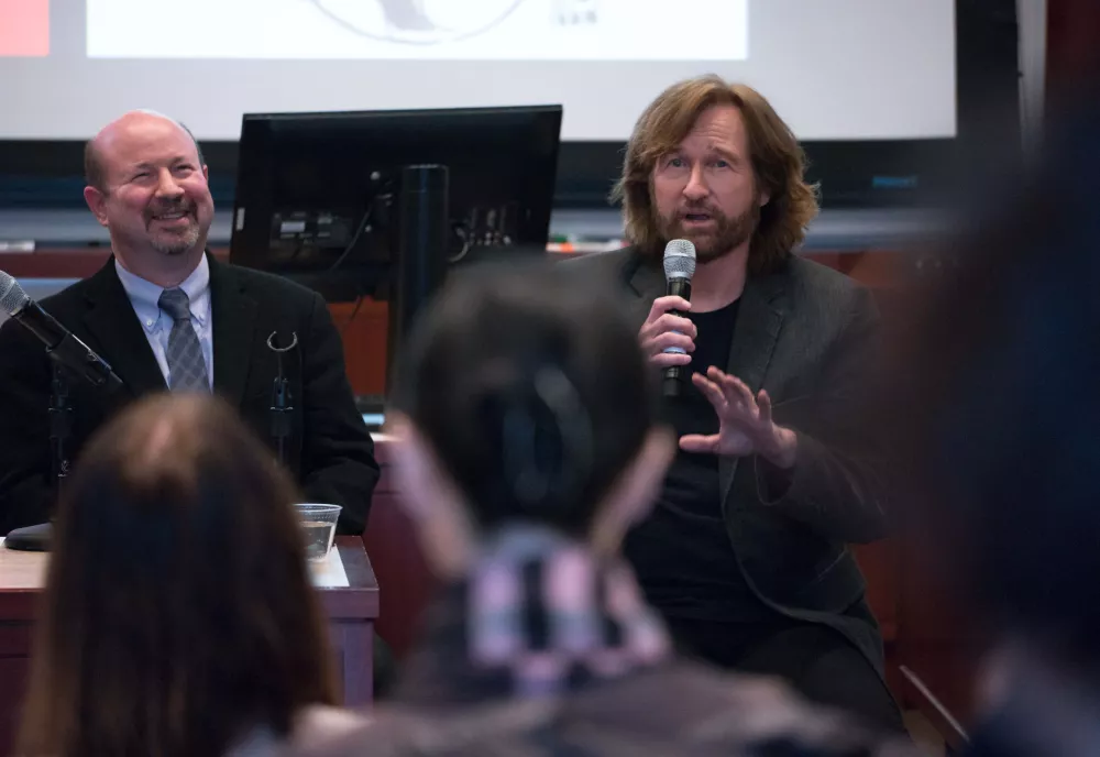 Mann and Toles introduce themselves in front of a slide featuring The Madhouse Effect book cover and a cartoon of the pair with armed with their ‘weapons of choice.’