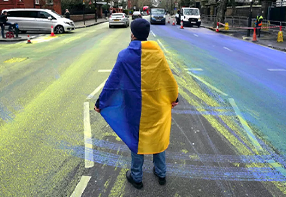 A person draped in the Ukrainian flag stands in a street awash with yellow and blue.