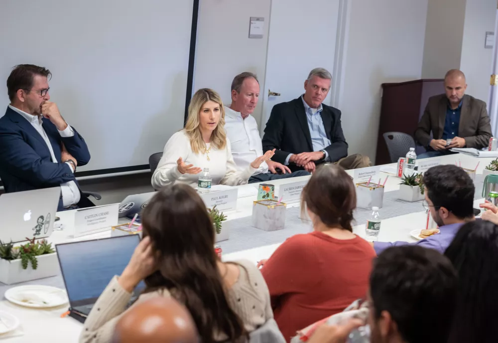 Lauren Zabierek speaks to a group of people seated around a table.