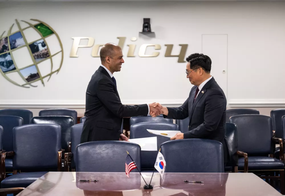 Vipin Narang shakes hands with Chang Lae Cho while standing next to a conference table with American and South Korean flags.