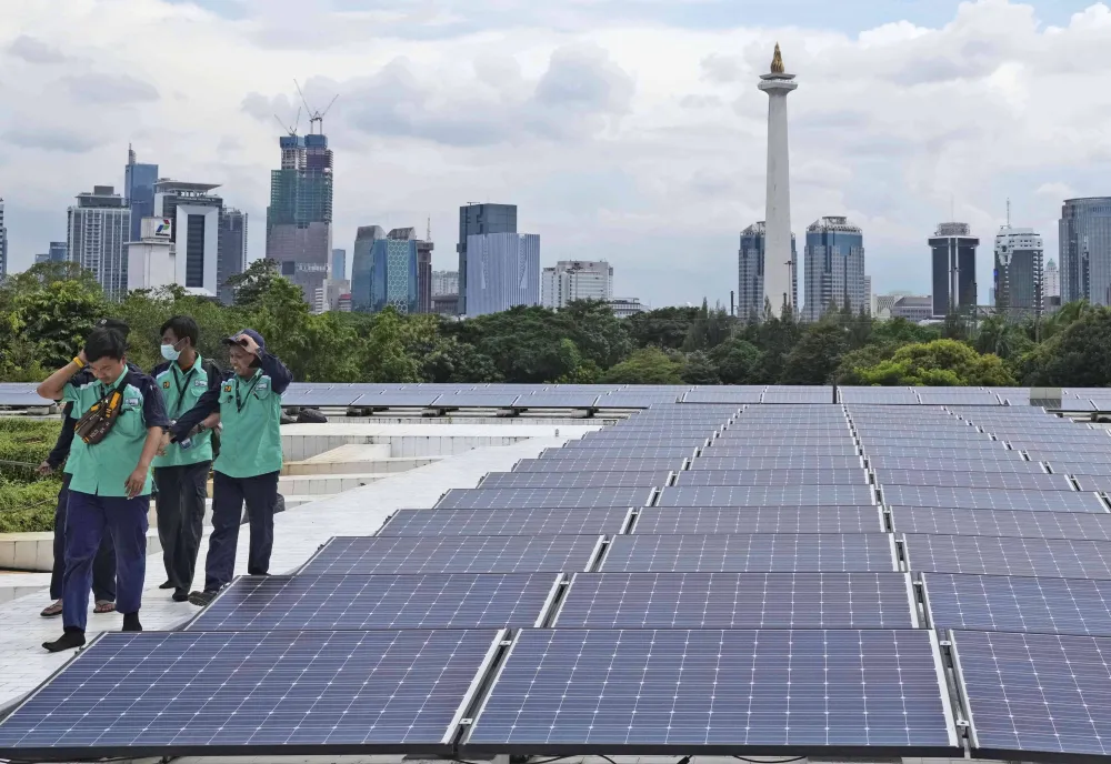Workers walk near solar panels that provide partial electrical power to Istiqlal Mosque as the city skyline is seen in the background, in Jakarta, Indonesia, Wednesday, March 29, 2023. (AP Photo/Tatan Syuflana)