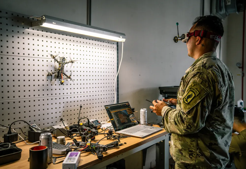 A soldier stands in front of a workbench testing a drone.