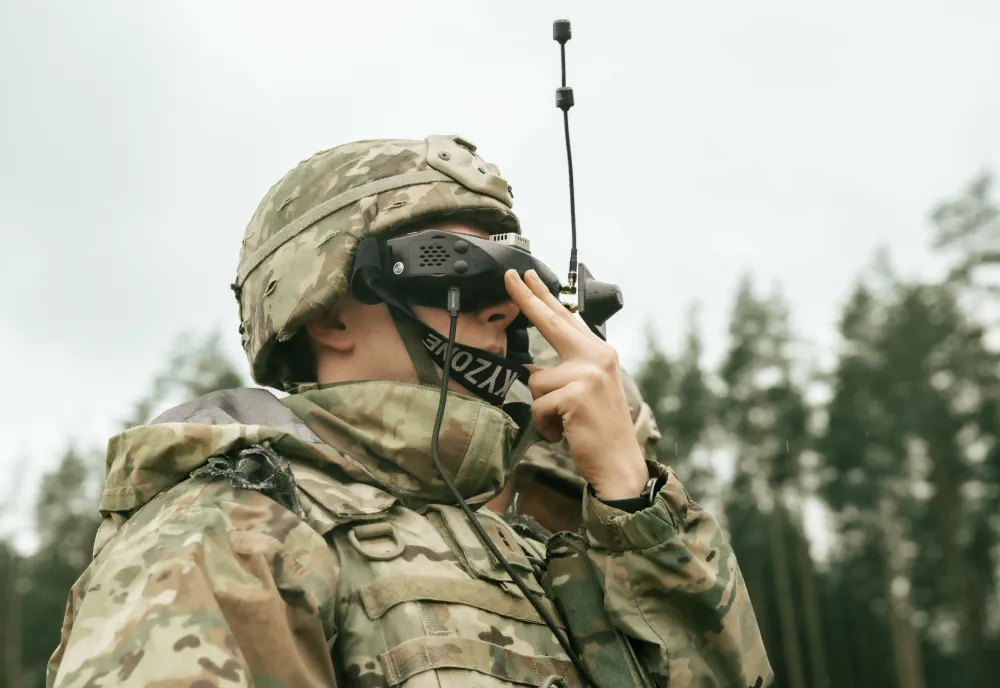 A soldier looks through first-person viewer goggles while flying a drone.