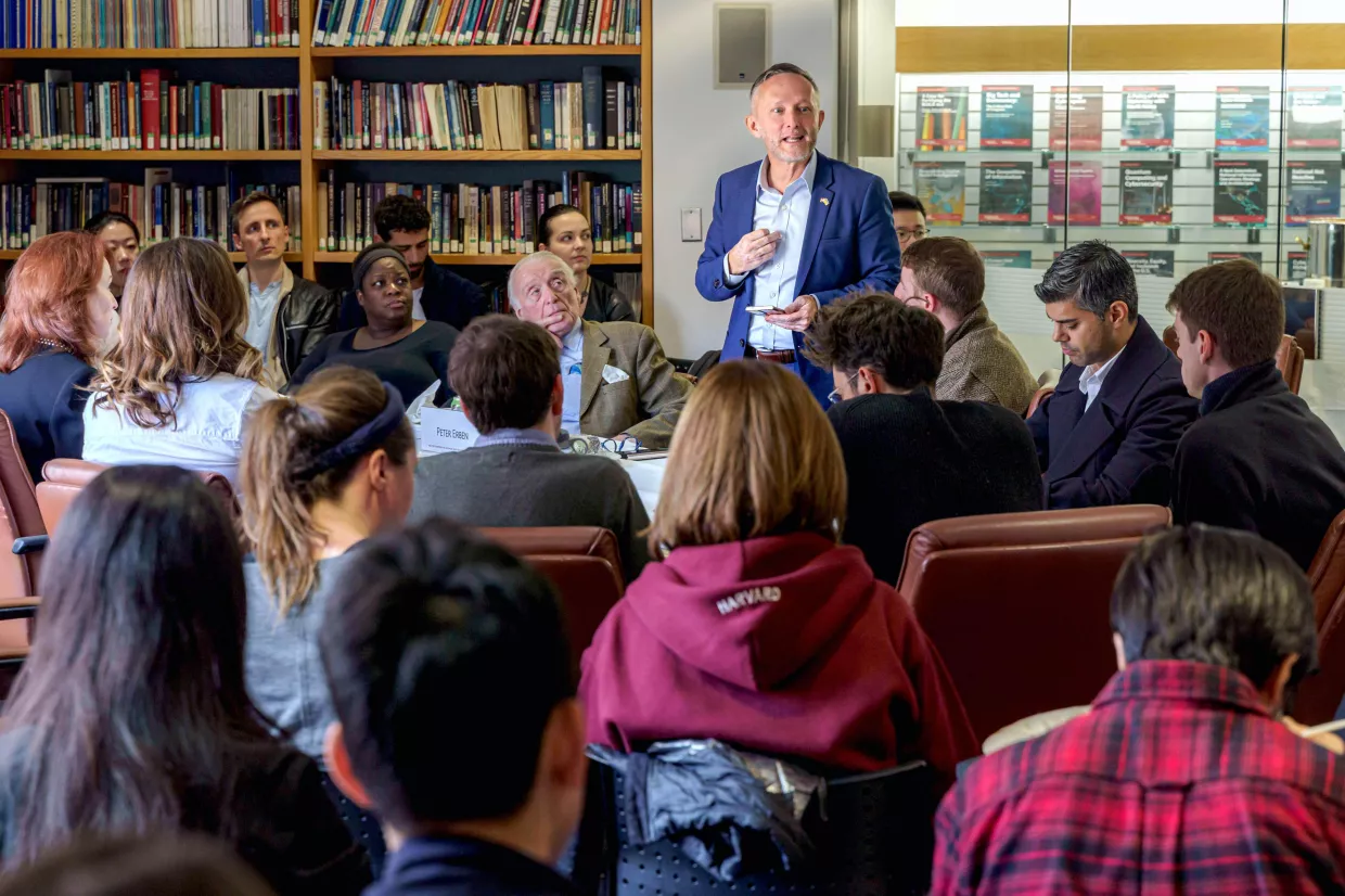 Peter Erben stands at the Belfer Library conference table surrounded by students. Seated across the table is Meghan O'Sullivan.