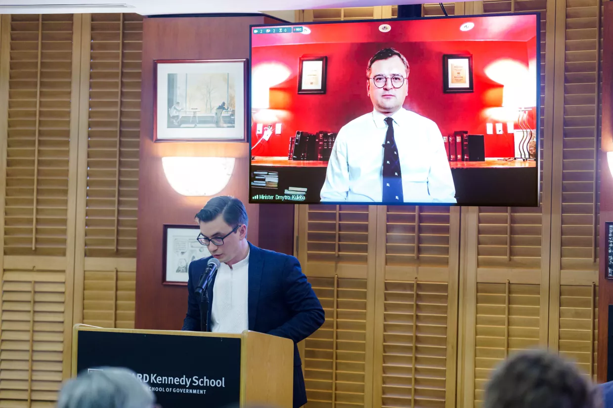 Ilya Timtchenko speaks from a podium with Dmytro Kuleba on screen behind him.