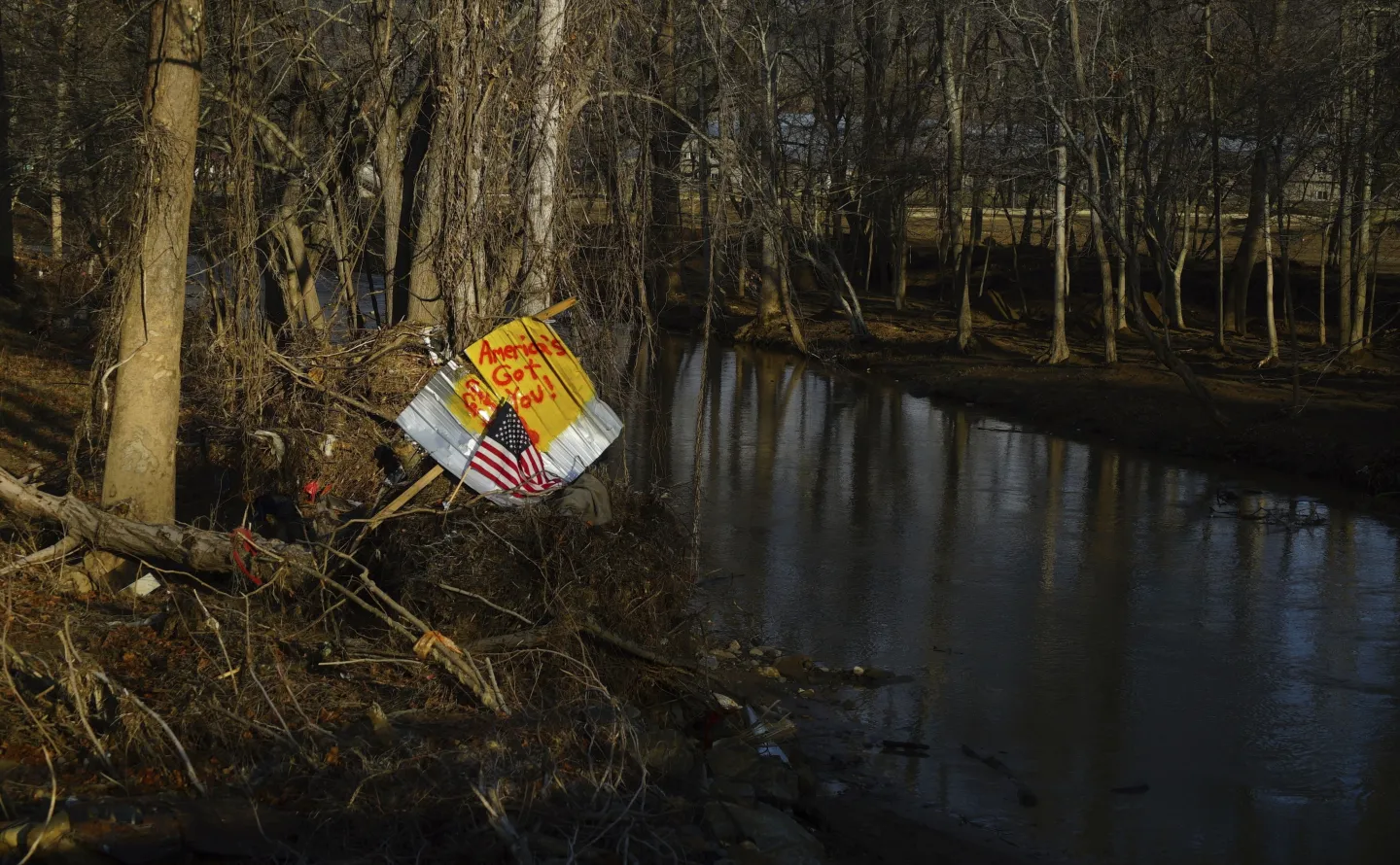 A piece of debris with an American flag and inspirational message stand along a riverbank in Swannanoa, N.C., on Friday, Feb. 7, 2025. More than four months after the remnants of Hurricane Helene devastated western North Carolina, many residents are frustrated with the federal response. (AP Photo/Allen G. Breed)