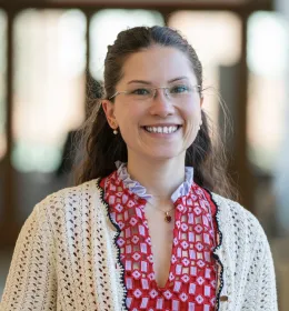 Woman in red dress with a white cardigan faces the camera, smiling.