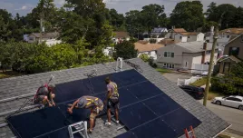 three workers install solar panels on roof of home