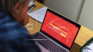A man sits in an office in front of a laptop that is infected with a fictitious encryption Trojan (ransomware). 