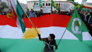 A Kurdish protester poses with a small Kurdish flag in front of a large Kurdish flag.