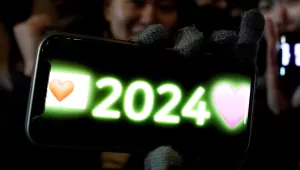 A woman poses for a photo with her smartphone displaying 2024
