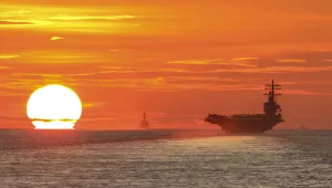 As the setting sun looms large across the South China Sea, it silhouettes an aircraft carrier in the foreground and other U.S. Navy ships in the distance.
