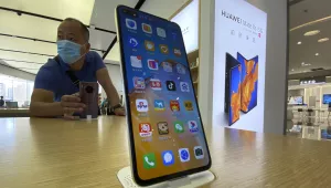 Photo of a visitor to a Huawei retail store stands near a Huawei smartphone displaying a variety of apps in Beijing on Tuesday, Sept. 8, 2020.