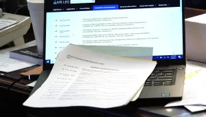 An open laptop on a messy desk. Papers covers the keyboard.