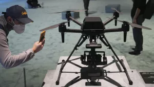 A person on the left bends to take pictures of a drone showcased on a platform on the right.