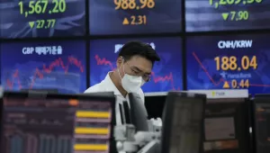 A currency trader sits in front of screens showing numbers of multiple national currencies.