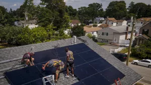 three workers install solar panels on roof of home
