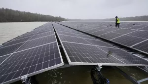 Man in hardhat walks between floating solar panels on a lake