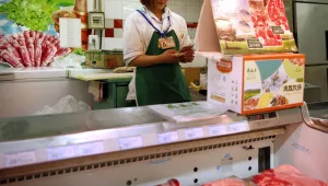 A clerk checks her smartphone near a display advertising domestically produced Chinese beef and lamb at a supermarket in Beijing, May 12, 2017. A new trade deal with the U.S. could help feed China's growing appetite for beef and increase natural gas imports but will likely make only a negligible dent in the U.S. trade deficit. (AP Photo/Mark Schiefelbein)
