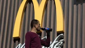 A Chinese worker drinks a U.S. brand soda near a U.S. fast food restaurant in Beijing, China, Tuesday, November 7, 2017. (AP Photo/Ng Han Guan)
