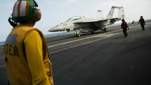 Crew member looks at a taxing F/A-18 fighter jet on the deck of the USS Abraham Lincoln aircraft carrier