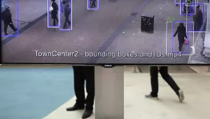 People walk behind a screen which shows a prototype of a program developed by ML6 technology which can track people walking in a street during an innovation and technology fair.