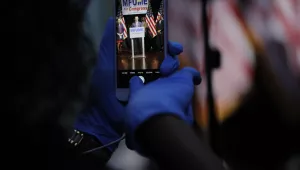 A staff member in the Kweisi Mfume campaign uses gloves while holding a cell phone during an election night news conference at his campaign headquarters after Mfume, a Democrat, won Maryland’s 7th Congressional District special election, Tuesday, April 28, 2020, in Baltimore.