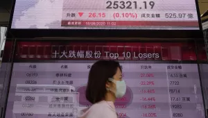 A woman wearing a face mask walks past a bank's electronic board showing the Hong Kong share index at Hong Kong Stock Exchange Tuesday, Aug. 18, 2020. 