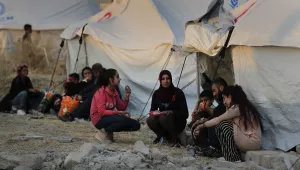 Displaced Syrians wait outside tents.