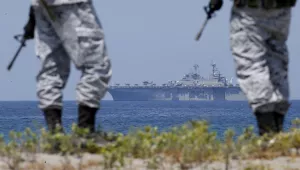 Solider stand on shore with naval ship in the distance