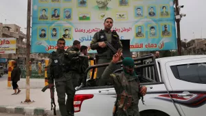 In this photo taken on Wednesday, March 28, 2018, members of the Kurdish internal security forces stand on their vehicle in front of a giant poster showing portraits of fighters killed fighting against the Islamic State group, in Manbij, north Syria. Manbij, a mixed Arab and Kurdish town of nearly 400,000, was liberated from Islamic State militants in 2016 by the YPG fighters with backing from U.S-led coalition airstrikes. With Turkey's threats, the town has become the axle for U.S. policy in Syria, threate