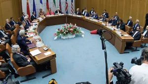 U.S. and Iranian negotiators sit around a cured table as media with cameras and microphones crowd the foreground.