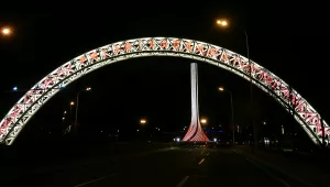 Gate of Tianjin Free-Trade Zone. A brightly lit arch over a nighttime roadway. A brightly lit pillar appears in the background.