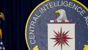 A large CIA seal to the right of an American flag on a flagpole topped with a gold eagle finial.