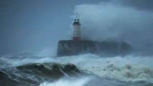 A lighthouse, battered by waves, sits at the center of this dark and stormy seascape.