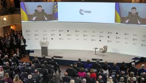 A wide shot of a crowd watching two large video screen with Ukraine President Zelenskyy on them at the Munich Security Conference