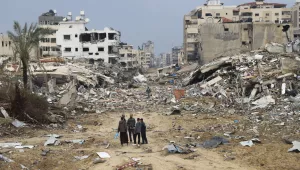 Palestinians walk past the building destroyed in the Israeli Bombardment of Gaza (AP Photo/Mohammed Hajjar)