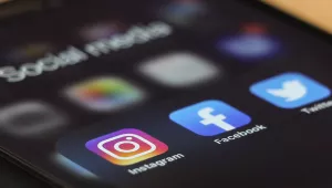 A mobile phone displaying the icons of Instagram, Facebook, and Twitter.