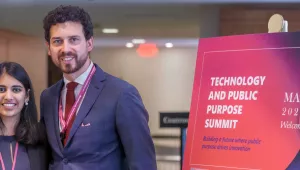 Two people stand next to a sign that says Technology and Public Purpose Summit