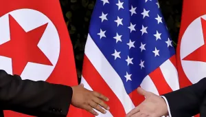 two hands reaching to shake in front of U.S. and North Korean flags.