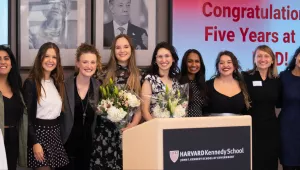 Women line up in front of a screen reading "congratulations on five years at HKS"