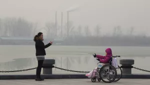 Visitors in a park gesture at each other near chimneys spewing smoke in Beijing, China