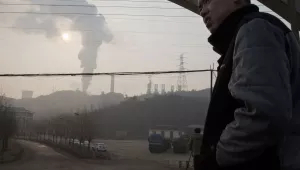a man looks up near smoke spewing from a chimney near the Jiujiang steel and rolling mills in Qianan