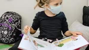 A girl wearing a mask reads a book in a classroom.