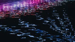 Neon lights reflect off rippling water.