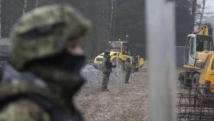 Military watching the start of work on the first part of some 180 kilometers of a 5.5 meter-high metal wall