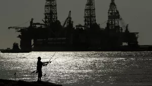 A man fishes near an oil drilling platform 