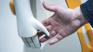 A human hand reaches out to shake the hand of a PAL robot.