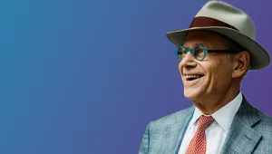 Richard Sandor, a smiling older white man wearing a suit, fedora, and blue glasses.
