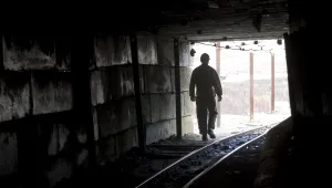 A miner is silhouetted at the mouth of a dark mine tunnel.